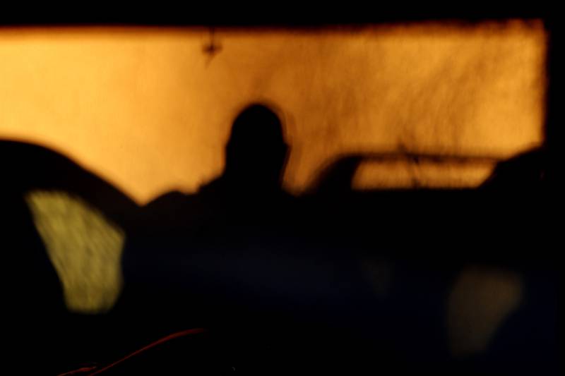 The shadow of a man getting into a car is cast on the wall by the sun.