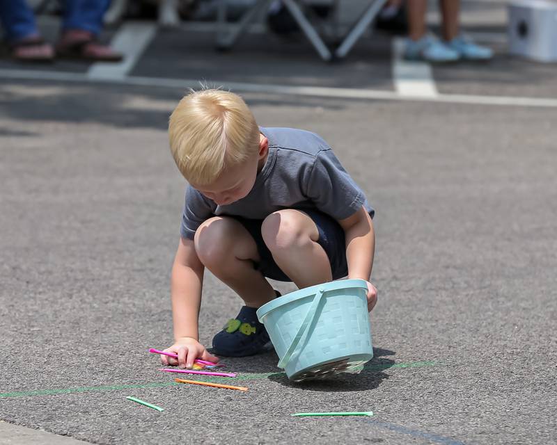 A little boy collects candy left on the street at the annual PrairieFest parade in downtown Oswego. June 18, 2023.