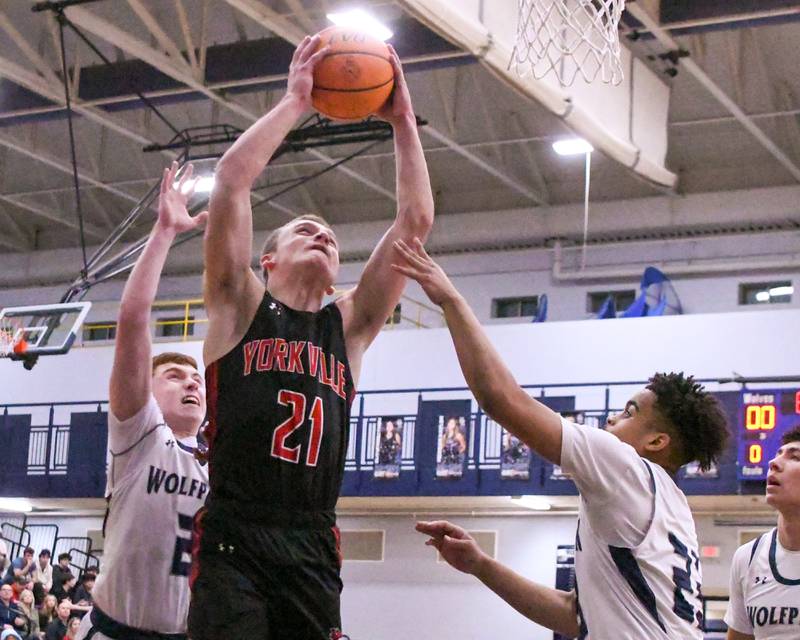Yorkville's Taelor Clements (21) makes a basket while being defended by Oswego East's Torrin Ross (23) and Oswego East's Brady Roberts (2) during the game on Friday Feb. 14, 2025, held at Oswego East High School.