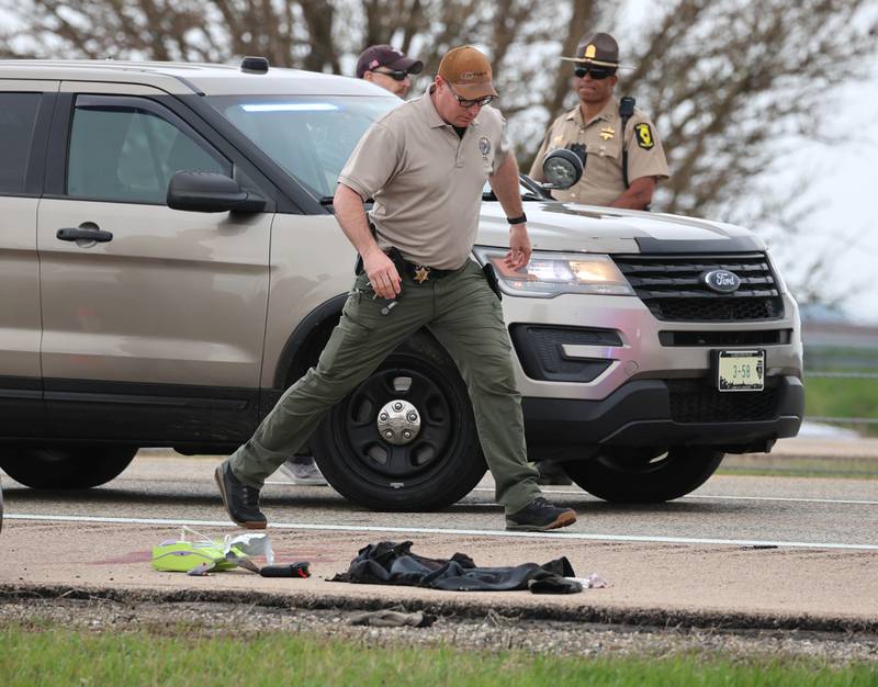 An Illinois State Police crime scene investigator steps around some debris, clothing and apparent blood near a Honda sedan with a shattered window Monday, April 27, 2026, in the westbound lanes of Interstate 88. Police were investigating an incident on I-88 just west of Keslinger Road in Maple Park.