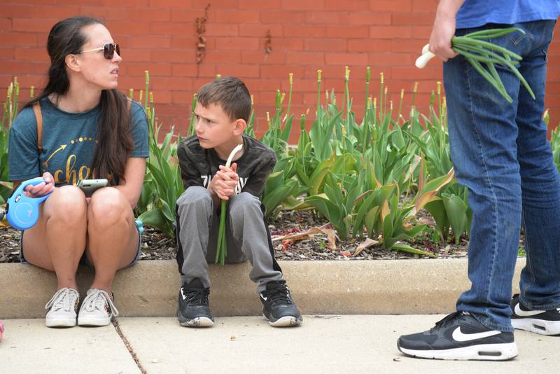 Ethan McConkey of Downers Grove eats a raw onion beside his mother Jennifer McConkey while they attend the Downers Grove Farmers Market Saturday May 13, 2023.
