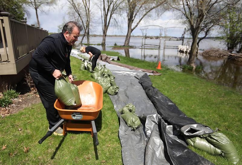 Ken and Robyn Kilberger work on installing sandbags to protect their home from flooding on Sunday, April 19, 2026, in Johnsburg, as the Fox River continues to rise.