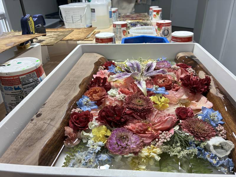 Tina Bupp pours one shallow layer of resin at a time to preserve dried flowers at McHenry's Bupp Woodworks & Designs, seen here on Nov. 28, 2025.