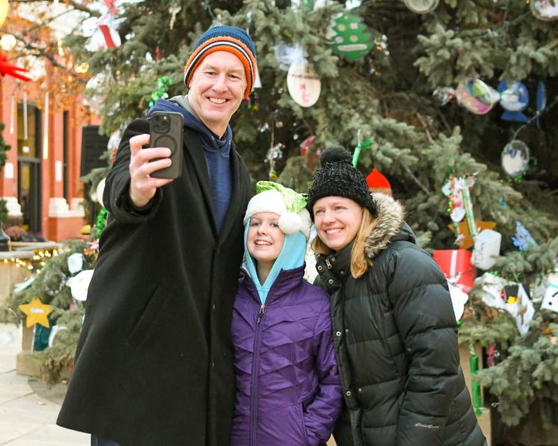 John Curran along with his wife Sue Curran and daughter Rachel, 10, of Downers Grove take a photo on Friday Nov. 29, 2024, in front of the tree before the Christmas tree lighting ceremony in downtown Downers Grove and come to listen to a family member in the Downers Grove South Marching band preform during the event.
