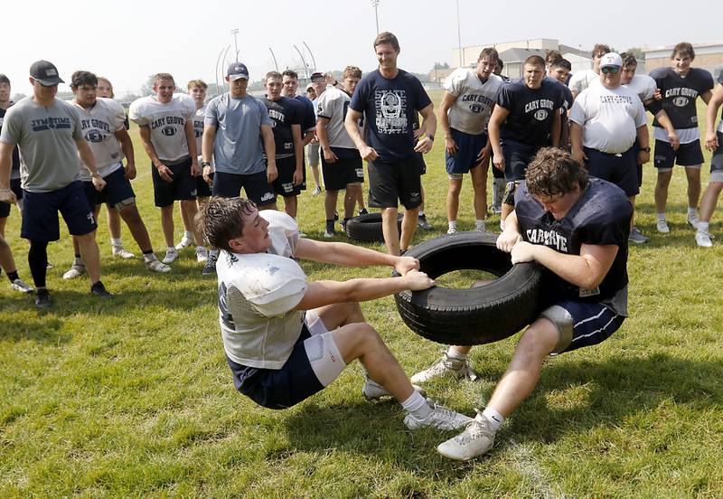 Cary-Grove players cheer for their teammates as Jack Rocen (left) and Ethan Hammer compete in tire tug-of-war during football practice Thursday, June 29, 2022, at Cary-Grove High School in Cary.