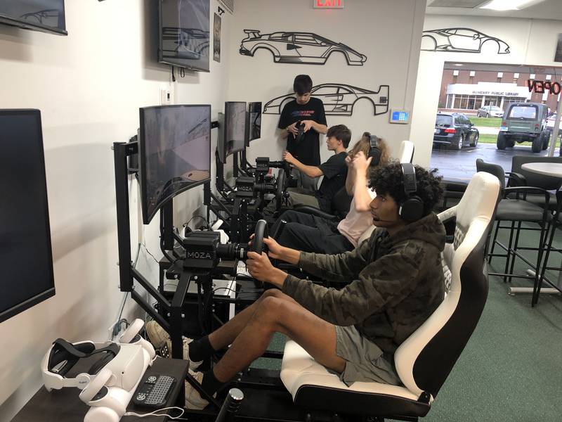 Jamicko Hernandez, Angelo Breslin and Nolan McDaniel race on the same virtual track at RaceTime VR Racing and Escape Rooms in McHenry on Thursday, Oct. 19, 2023. Kaleb Rice, standing, is the son of owners Jim and Jen Rice and helped his father build the virtual reality racing rigs.