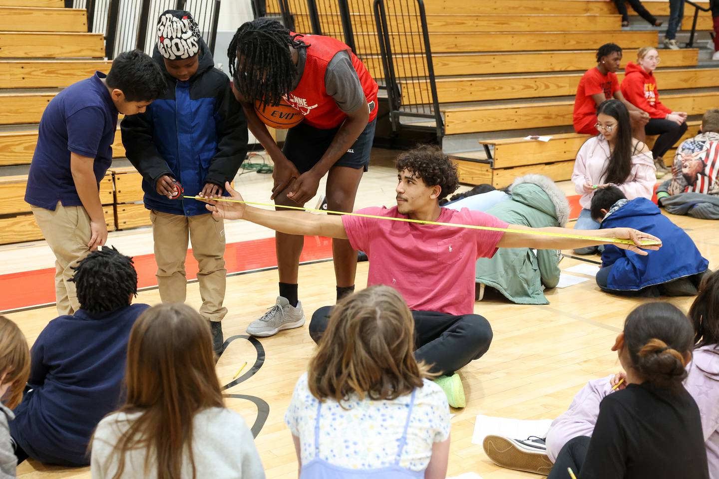 Grade school students measure the wingspan of St. Anne High School basketball player Deion Fifer as part of their math worksheet during the district's Math Madness held on March 20 at the high school.