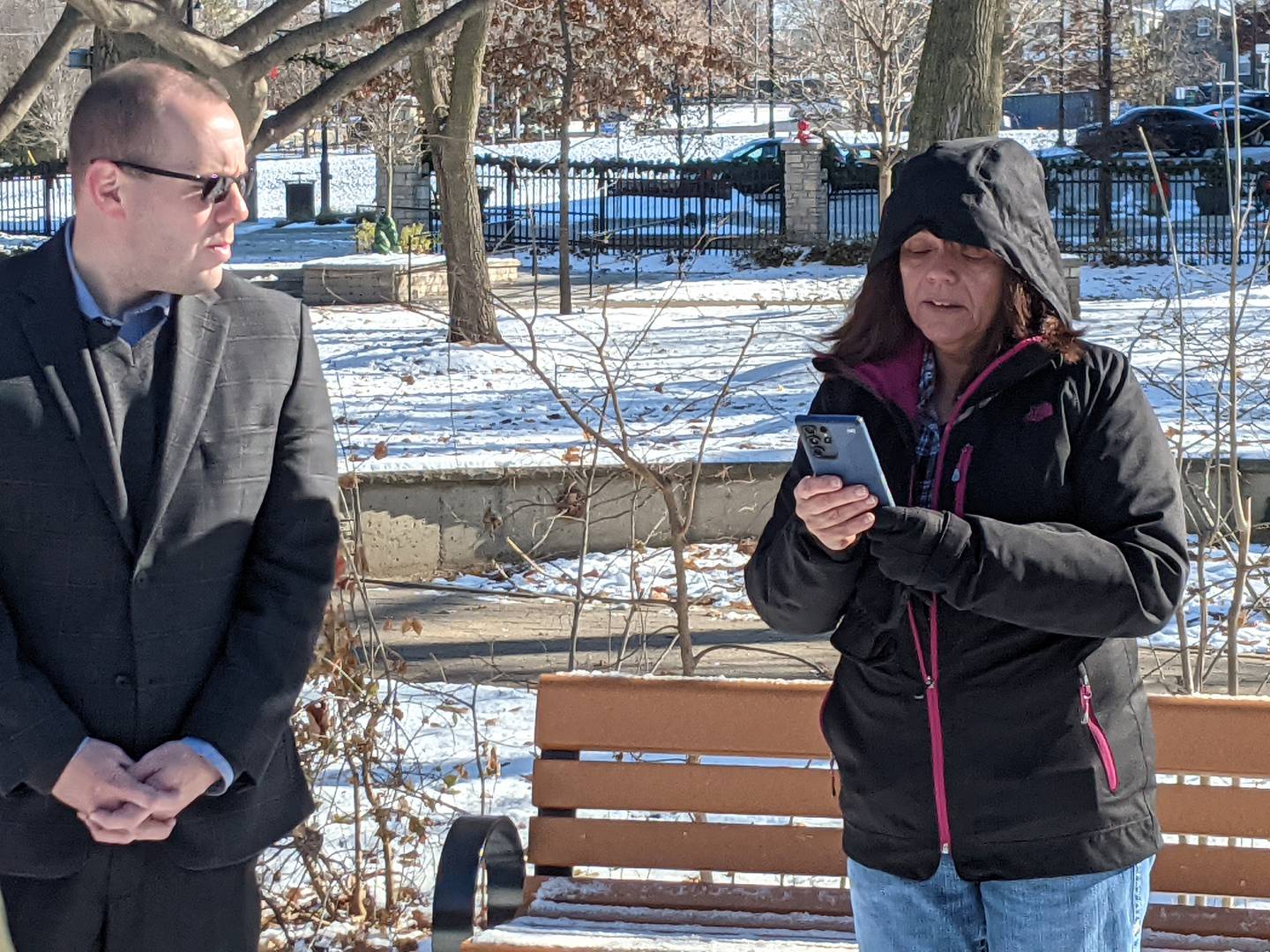 Oswego Village President Ryan Kauffman, left, listens as Marg Esposito, right, the aunt of Oswego resident Amanda Zentmyer Olson, reads a poem as part of a ceremony on Nov. 28 dedicating a memorial bench at Hudson Crossing Park in downtown Oswego in Olson's name.