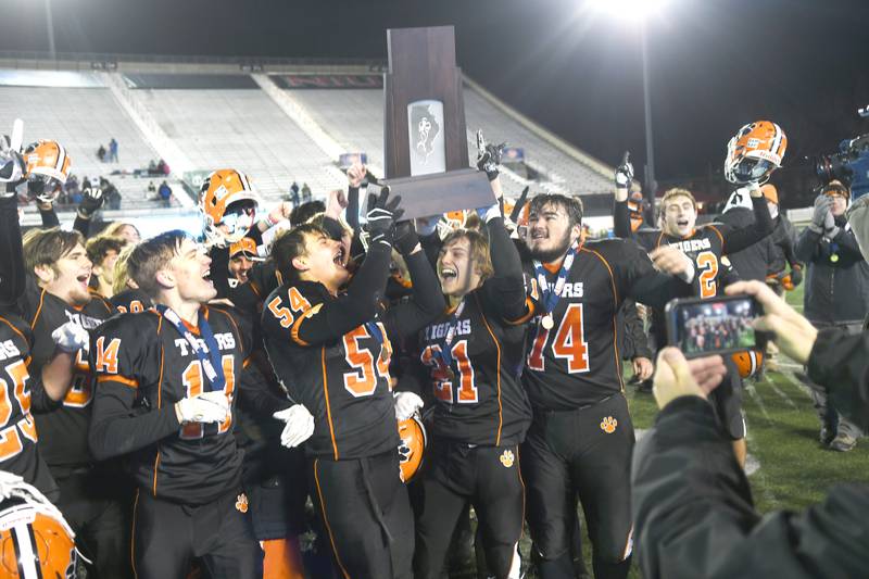 Byron seniors Ethan Palzkill (14), Jake Lenz (54), Chandler Binkley (21), and Nick Brass (74) celebrate as they hoist the 3A championship trophy after defeating Tolono Unity 35-7 at Huskie Stadium in DeKalb on Friday.