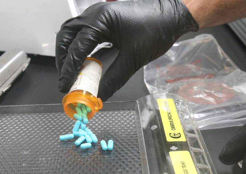 La Salle County Corner Rich Ploch, dumps medication pills onto a hazardous drugs tray inside a filter balancing containment hood at the La Salle County Forensic Center on Wednesday, Aug. 30, 2023 in Oglesby. The hood balances exposures of fumes and other particulates containing powders and removes toxic particulate and other matter when handling the material. State statute requires corners to use machines like this after collecting the medication from the scene of a death.