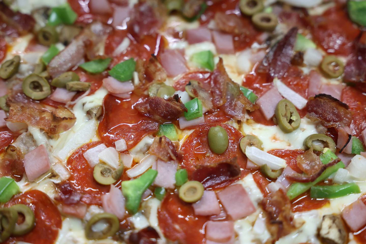 Sopranos Pizzeria and Catering, in Lockport, supreme pizza is prepared with the toppings on top with ham and bacon instead of the traditional sausage along with pepperoni.