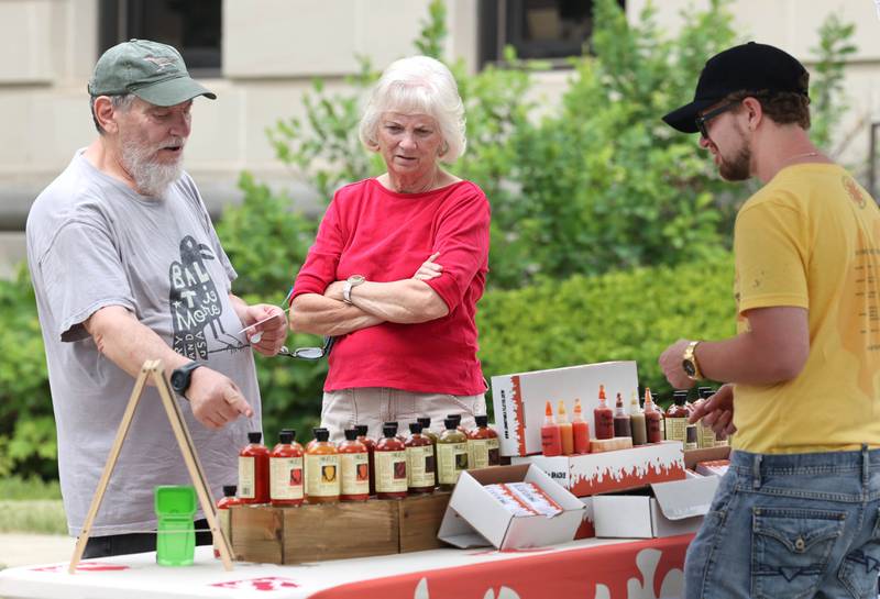 Randy and Bessie Kraut, from Schaumburg, make a purchase from from Cody Woodraska, a salesman at the Chef Heatley’s Hot Pepper Farm tent, Tuesday, June 6, 2023, at the Sycamore Farmers’ Market, on the lawn of the DeKalb County Courthouse.