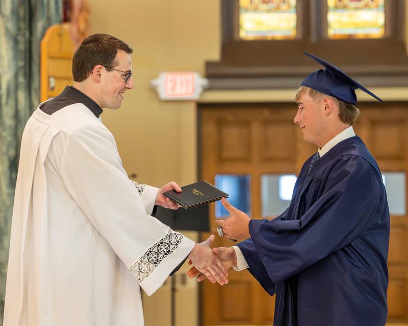 Father Nicolas Wilson hands diploma to Class of 2026 Marquette Academy Graduate during ceremony on May 24, 2026 at St. Columba Church in Ottawa.