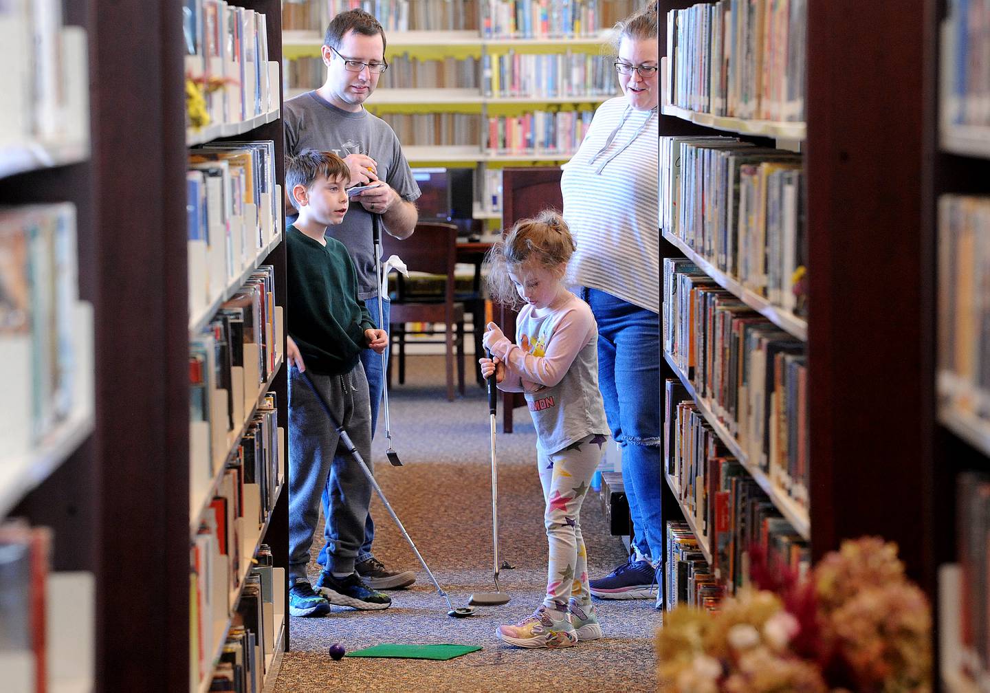 Parents Mike and Lauren Johnson and brother Liam, 8, watch Piper, 5, of Yorkville, take her shot on a hole between the upstairs stacks during the Friends of the Yorkville Library's annual Mini Golf FUN Raiser on Sunday Feb. 5, 2023.