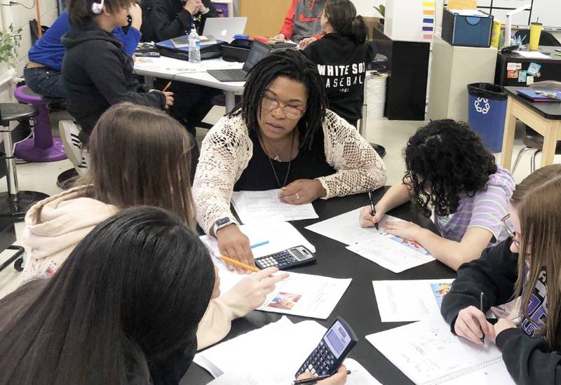 Sydney Hackley pulls up a seat to help a table of students with their classwork at Plano Middle School on Tuesday April 4, 2023.