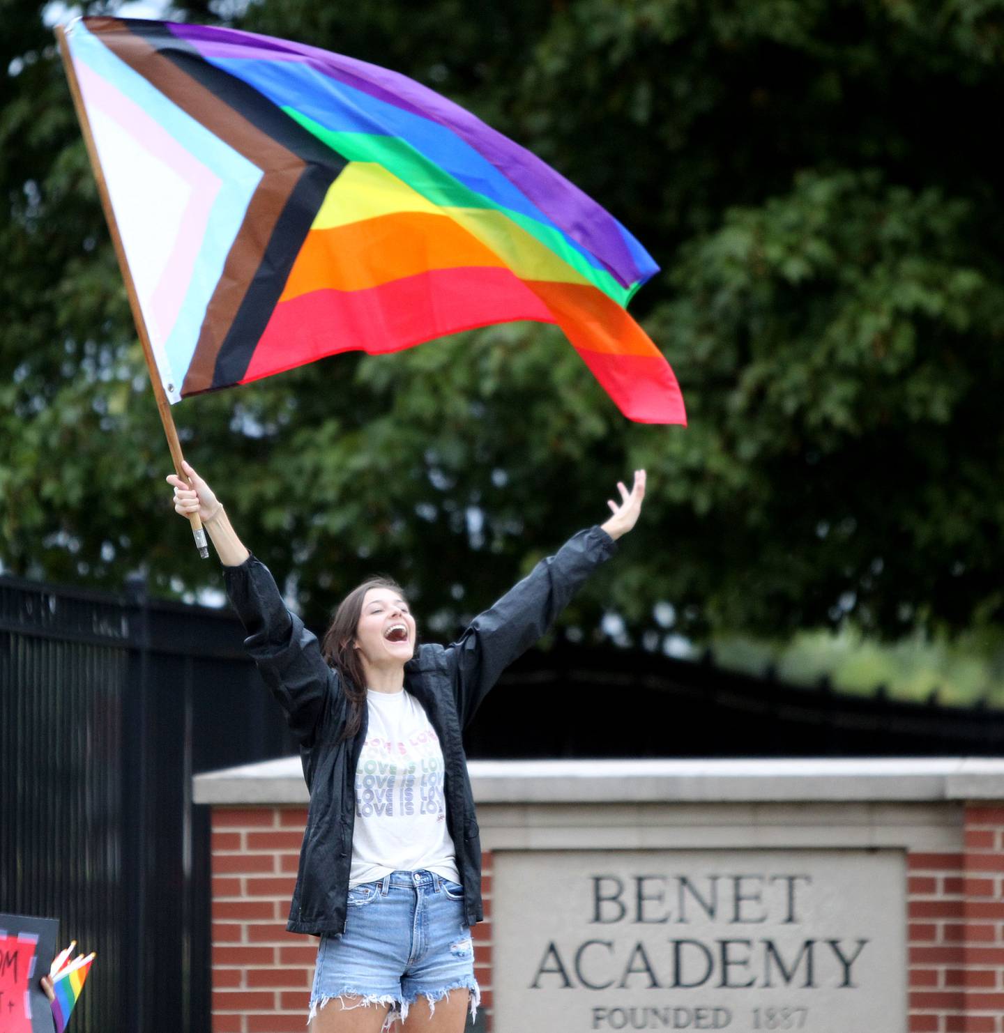 Benet Academy alumnus Annie Jacklich waves a rainbow flag outside the Lisle Catholic school in response to administrators rescinding an employment offer to the new girls lacrosse coach after learning that she was gay. The school reportedly hired Amanda Kammes, a Benet alum and head girls varsity lacrosse coach at Montini Catholic High School in Lombard, but rescinded the offer when her paperwork included her wife’s name as her emergency contact.