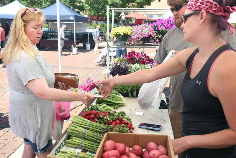 Kat Shell, (left) from Earlville, makes a purchase at the Theis Farm Market booth Thursday, June 2, 2022, during the first DeKalb Farmers Market of the season at Van Buer Plaza in Downtown DeKalb.