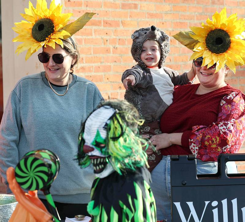 Willrett Flower Company owners Kat Willrett (left) and her sister Mary Grace McCauley hand out candy as McCauley’s son Frank, 2, checks out the costumes in front of their shop in downtown DeKalb Thursday, Oct. 27, 2022, during the Spooktacular trick-or-treating event hosted by the DeKalb Chamber of Commerce.