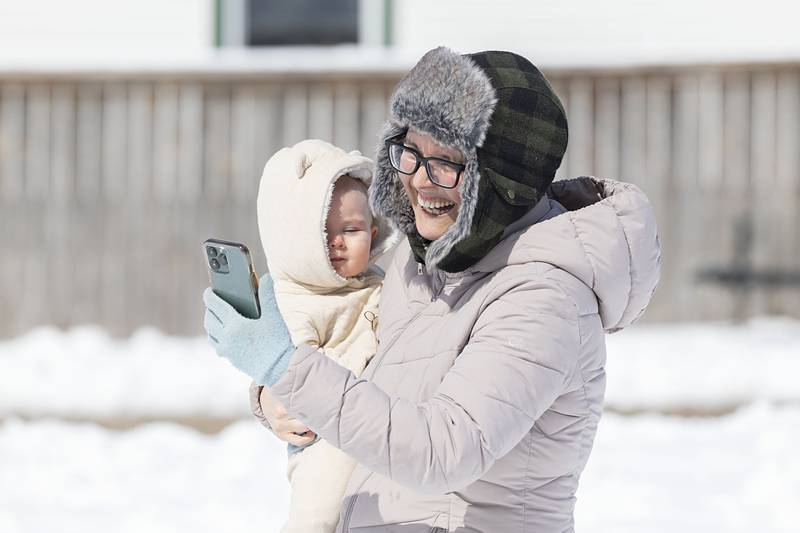 Cassondra DeLancey smiles while holding daughter Maddie, 9 months, while taking video of her family sledding Monday, March 16, 2026, at EC Smith Park in Dixon.
