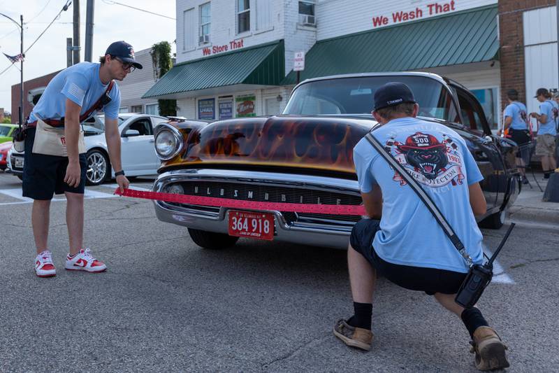(left to right) Firefighters Brady Benton and Trey Thomas measure out tickets in front of a car at the 20th annual Cruise Night on Friday, August 8, 2025, on Main Street in Marseilles.