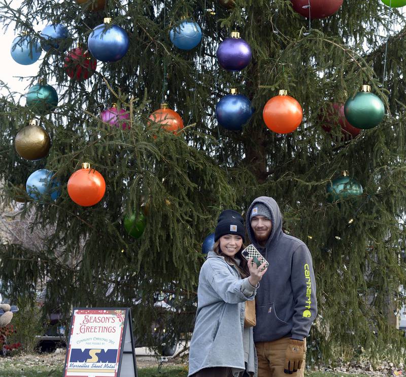 Taylor Weymouth and Dylan Limon take a selfie Saturday, Nov. 30, 2024, in front of the city Christmas tree at the Chris Kringle Market on the Jordan block in Ottawa. Scattered throughout downtown are several  S(Elfie) stations where visitors can satisfy their holiday photo desires.
