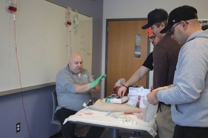 Illinois Valley Community College EMS instructor Nick Fish (left) with students Tyler Walsh, Dylan Kimak and Brady Mitchell put on gloves prior to starting an intravenous line.