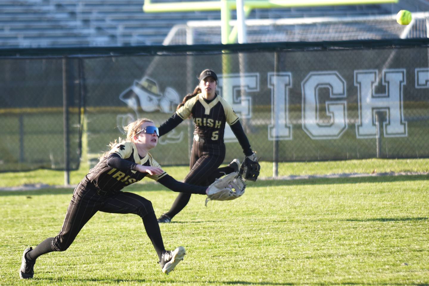 Bishop McNamara's Maddy Weiland dives for a fly ball she went on to catch as Vivian Dole looks on in the background during a home game against Peotone Monday, March 23, 2026.