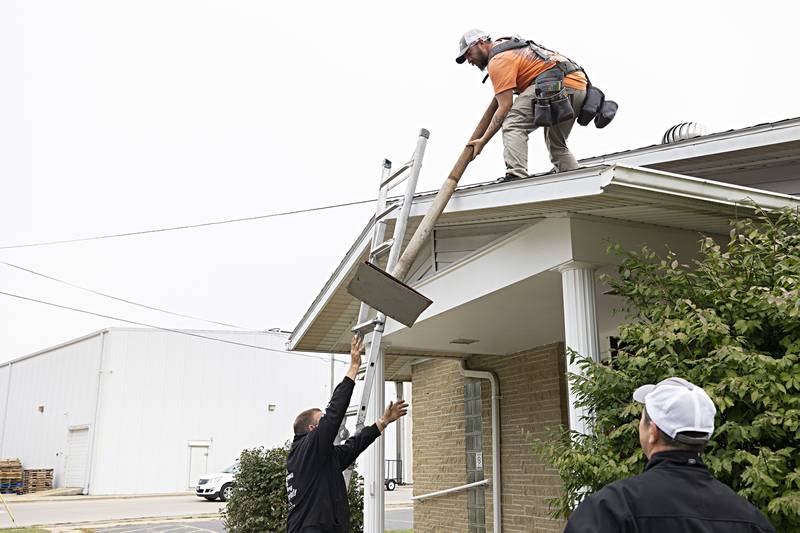 Adam Benford hands Keith Persico a heavy pipe used as a brace for the steeple from the roof Wednesday, Sept. 13, 2023.