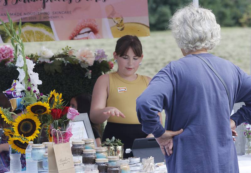 Sloane Descher, of Sloane’s Scrumptious Scrubs, tells a customer about her handmade nourishing skincare products during Pop Up Market outside of the Laskowski ACE Hardware store, in McHenry, on Friday, Aug.15, 2025, during McHenry.’ 815 Day.