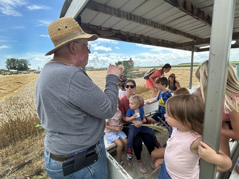 Roger Mixer of East Moline, shows kids how wheat is gleaned as a combine harvests a field in the background during a tour at the Bos Brothers Historical Farm south of Erie on Friday, July 25, 2025.