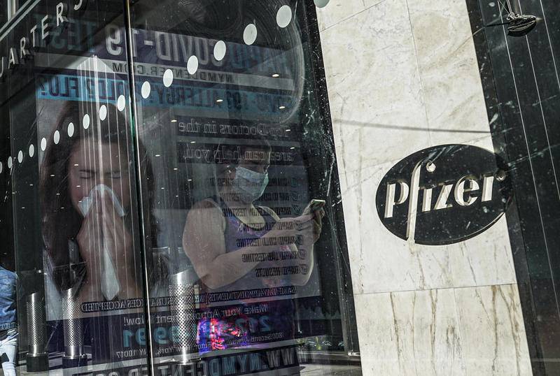 FILE - In this Nov. 9, 2020, file photo, an ad for COVID-19 testing reflects on glass at a bus stop, as pedestrians walk past Pfizer world headquarters in New York. On Friday, Nov. 20, 2020, Pfizer has asked U.S. regulators to allow emergency use of its COVID-19 vaccine, starting a process that could bring first shots as early as next month.  (AP Photo/Bebeto Matthews, File)