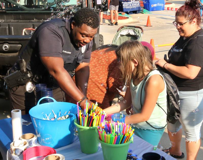 Rob Williams, a Sycamore Police officer, gives visitors a hand filling out raffle tickets Tuesday, Aug. 5, 2025, at the Sycamore Police Department booth during National Night Out in the Hy-Vee parking lot in Sycamore.