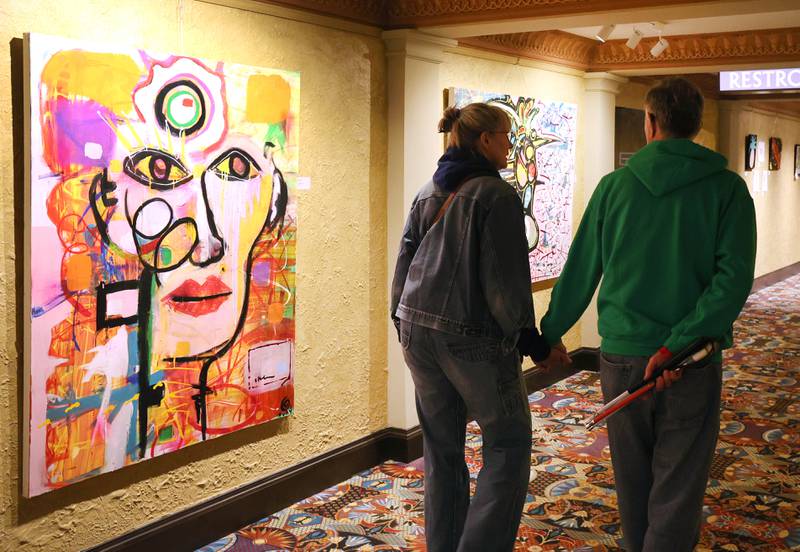 Visitors look at a paintings by Rudy Galindo during the Spring Art Exhibit opening reception Tuesday, March 22, 2022, at the Egyptian Theatre in DeKalb. The exhibit, featuring work from DeKalb County artists, runs until April 25.