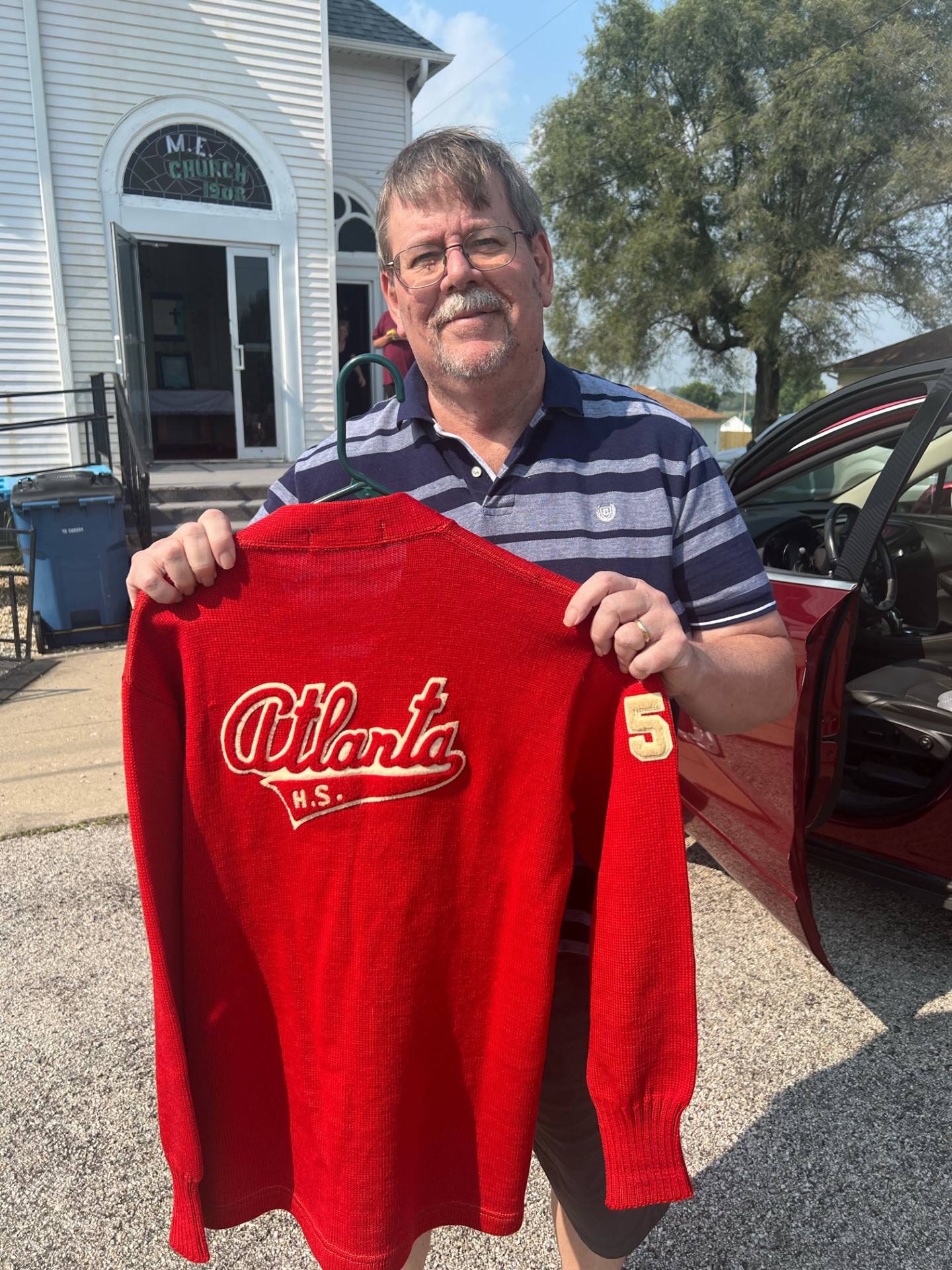 Bureau County Sports Editor Kevin Hieronymus holds the 1950 Atlanta High School Redwings letter sweater owned by his father, the late Dr. M. Lynn Hieronymus, at Saturday's Bureau County Basketball History event in Mineral.