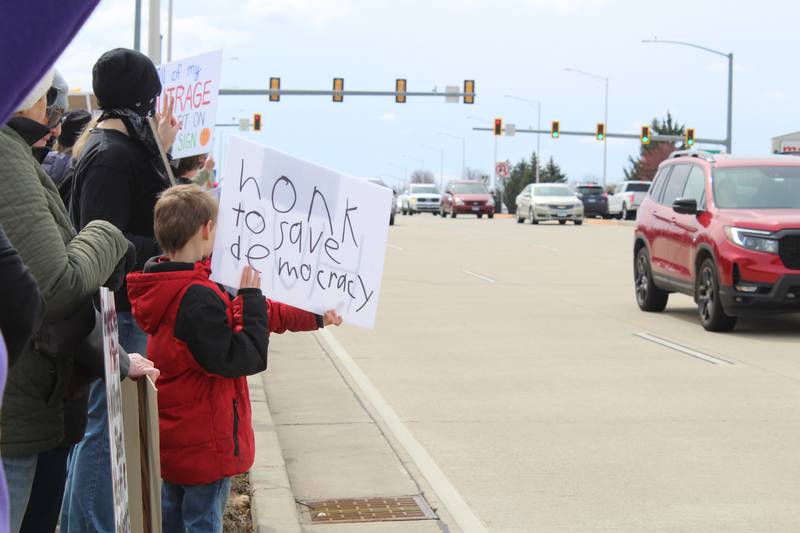 A child holds up a sign reading "Honk to save democracy" during the "Hands Off" protest along Randall Road in Algonquin on April 5, 2025.