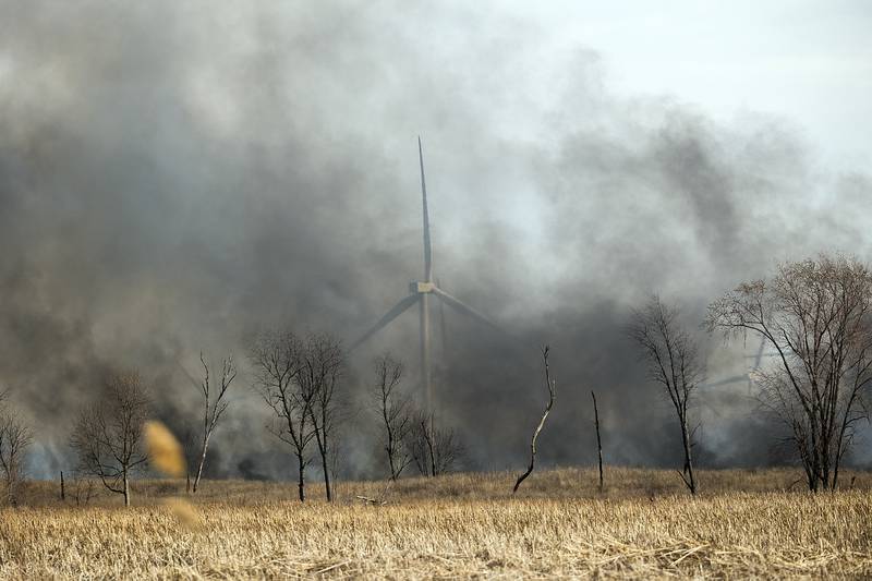 Dark smoke obscures a windmill Friday, March 14, 2025, as parts of Green River State Wildlife Area go up in flames.