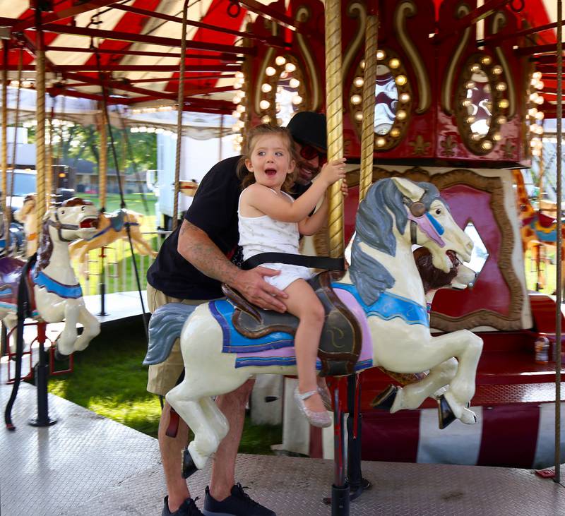 Matt Foster holds onto daughter Julia Foster as they ride the merry-go-round at the 2024 Sugar Grove Corn Boil on Friday, July 26, 2024.