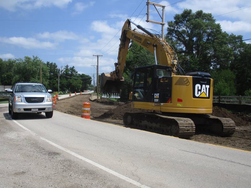 A westbound SUV rounds the Cannonball Trail curve in Yorkville on July 28, 2023 as an excavator digs into the roadway's subsurface in this view looking east.