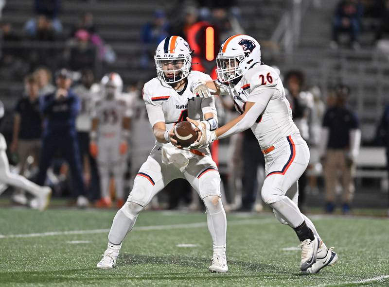 Oswego's Drew Kleinhans (4) hands the ball off to Dekker Zelensek during the conference game against Minooka on Friday, OCT. 10, 2025, at Minooka.
