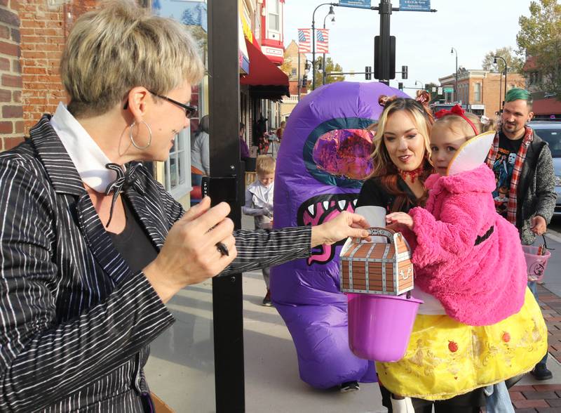 Svetlana Henrikson from There’s Fun In Store hands out a treat to Coraline Reed, 2, and her mom Valerie, from DeKalb, in front of the shop on Lincoln Highway in downtown DeKalb Thursday, Oct. 27, 2022, during the Spooktacular trick-or-treating event hosted by the DeKalb Chamber of Commerce.
