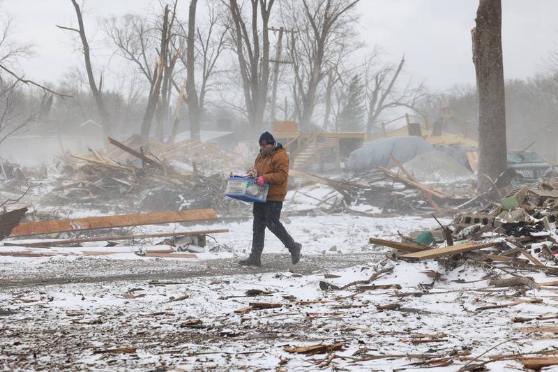 Near the summer home of Evanston residents Douglas Weber and Martha Plaza-Weber along South Sandbar Road in Aroma Township, their son-in-law Waldek Ziolkowski carries salvaged belongings from their demolished home a snow falls on March 16, 2026, following the March 10 tornado in Kankakee County.