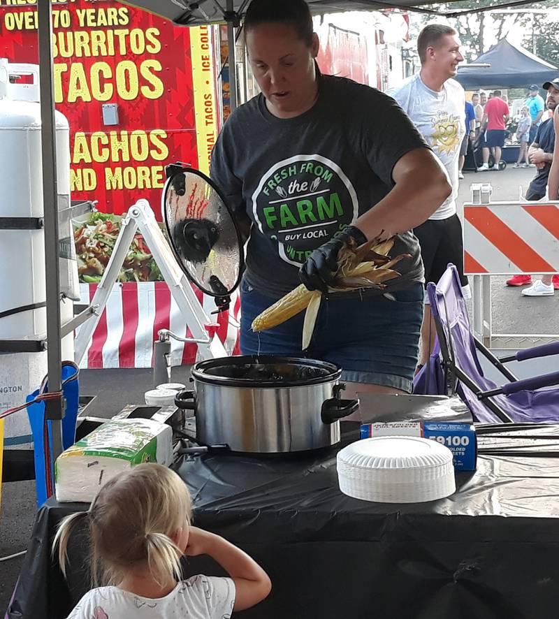 Kelsey Michelini-Brannan, of Country Kids in Peru, dips sweet corn in butter for a young onlooker Thursday, Aug. 4, 2022, during the opening night of the Taste of the Illinois Valley at Centennial Park in Peru.