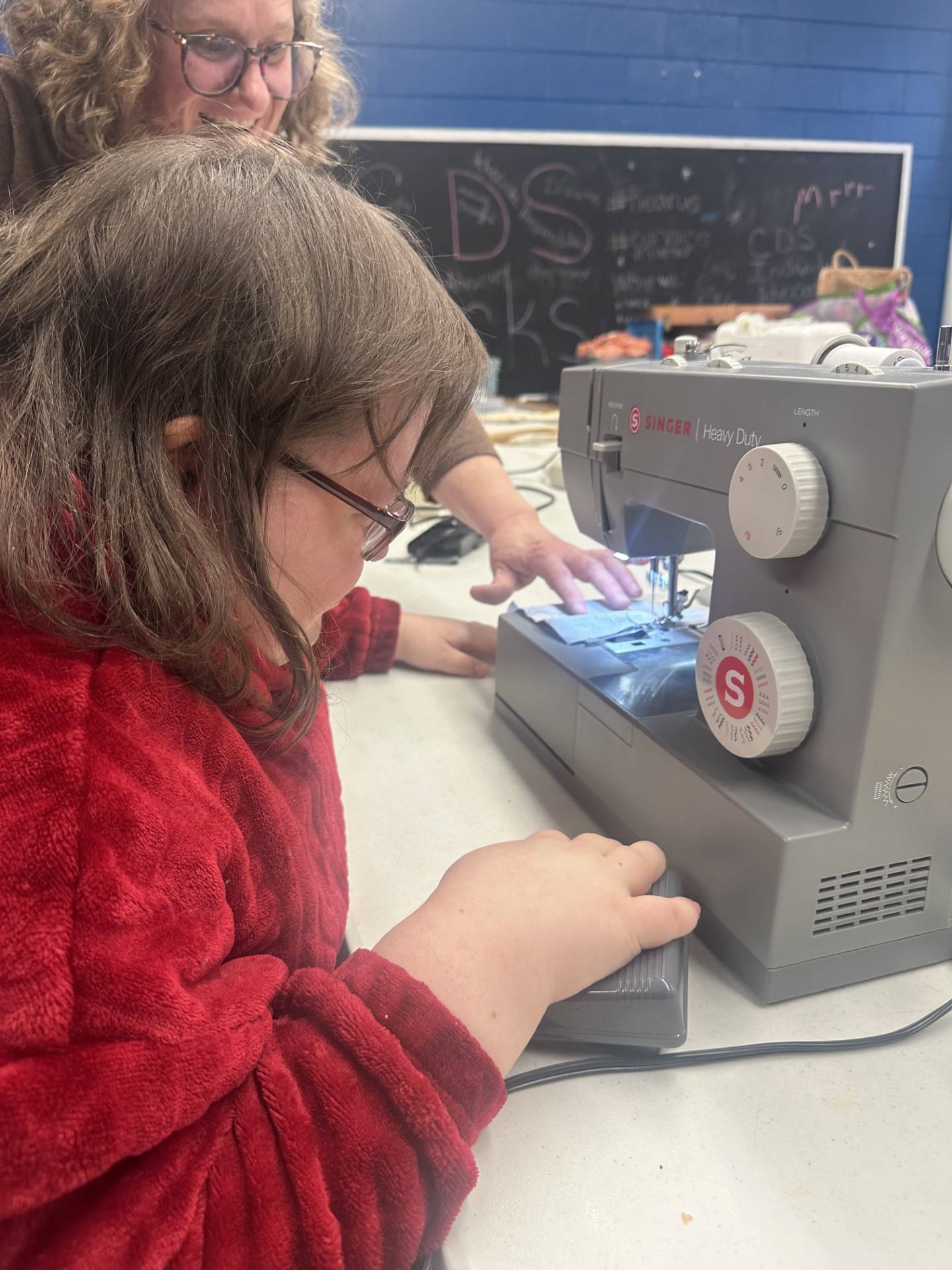 Kim Tillotson of Channahon, a UCP-Center for Disability Services board member and volunteer, shows new Sew What?! participant Angelica Cronin how to guide the fabric with her left hand as she uses her right hand to control the speed with the pedal.