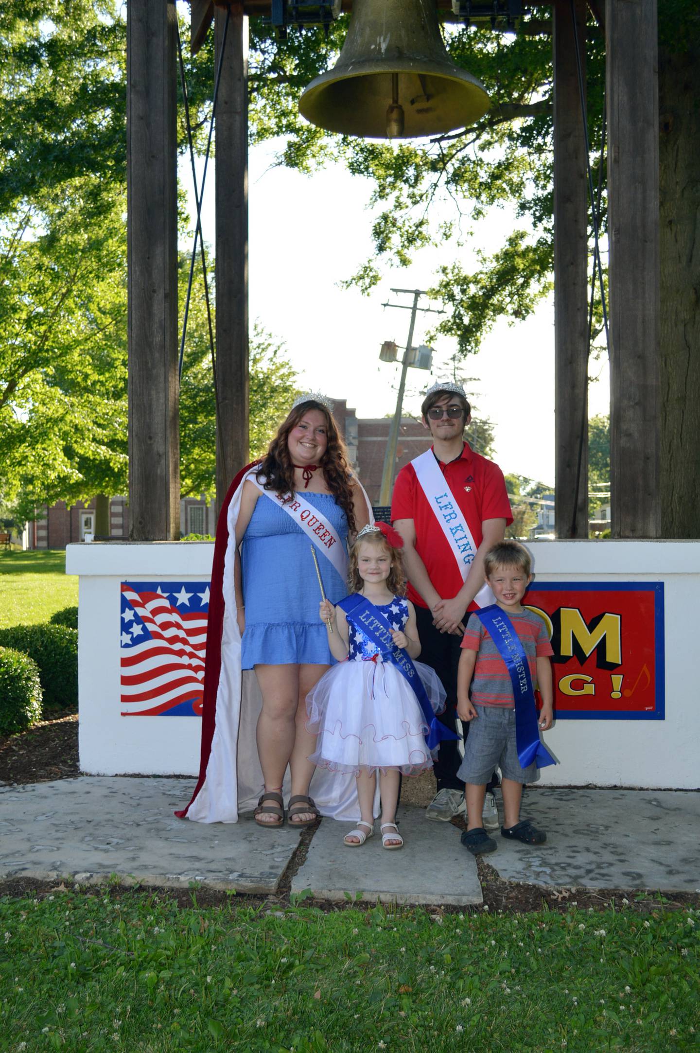 Let Freedom Ring Queen Abi Fletcher, back left, LFR King Immanuel Arellano, back right, Little Miss Firecracker Esther Skoumal, 5, front left, and Little Mister Firecracker Kamdyn Larson, 4, pose for a photo in front of the Illinois Freedom Bell on July 3, 2024.