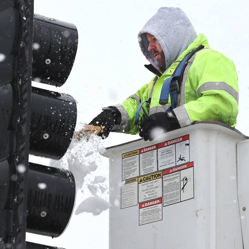 Kyle Krenz, an electrician with DeKalb Public Works, removes snow that has accumulated on the stoplights at the intersection of Lincoln Highway and Fourth Street Tuesday, Jan. 9, 2024, in DeKalb. Snow is expected to continue throughout the day with 7 to 10 inches of snow expected.