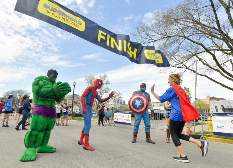 The Hulk, Spiderman, Captain America and Wonder Woman hi-five and cheer on runners as they cross the finish line of the Super Hero 5k Fun Run in Wheaton on Saturday, April 15, 2023.